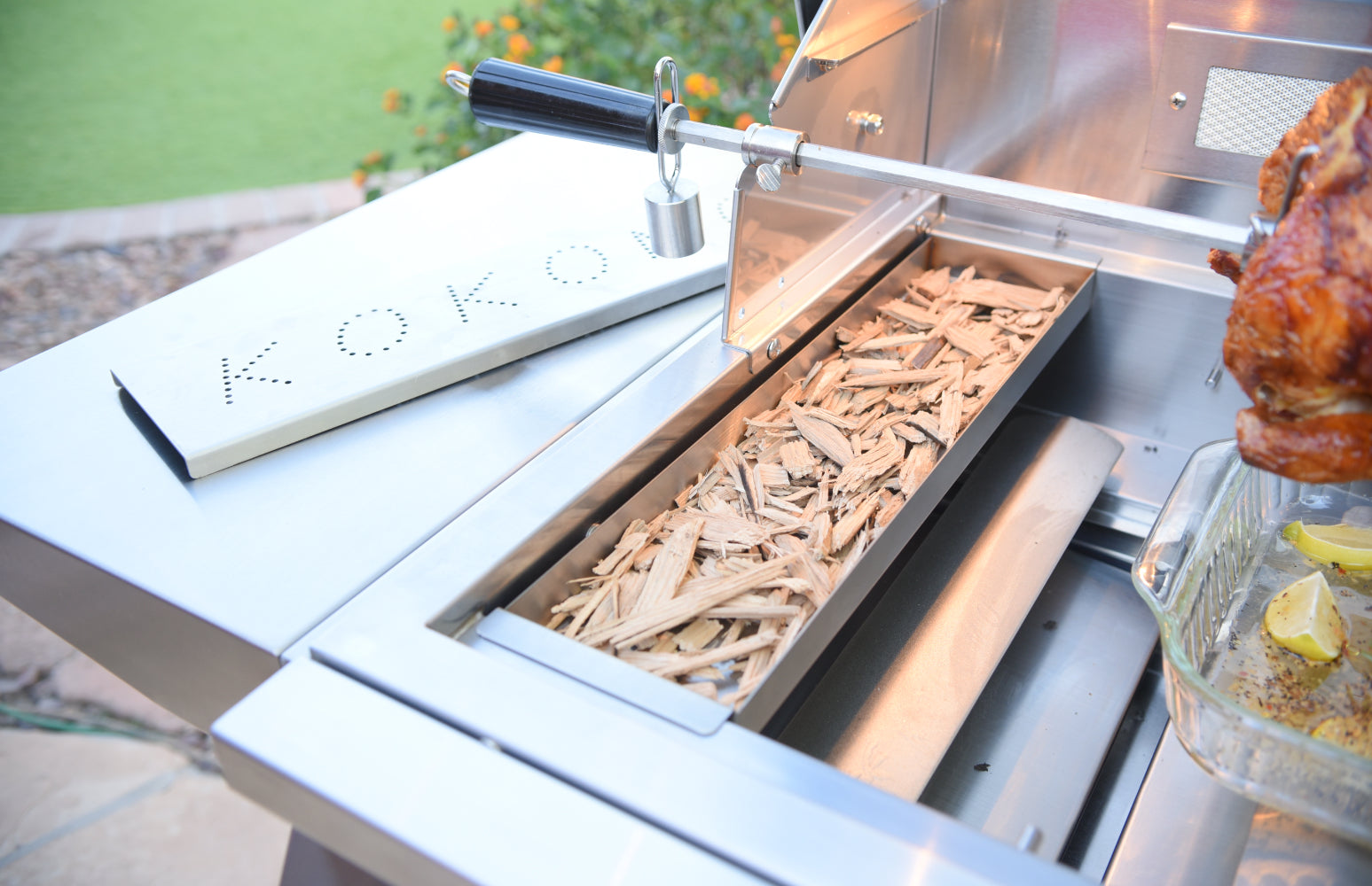 Grill with wood chips and a roasted chicken on a patio
