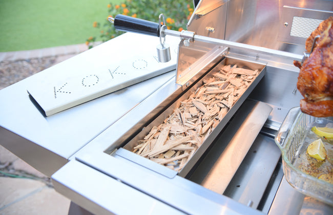 Grill with wood chips and a roasted chicken on a patio