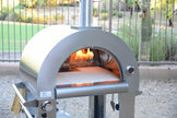 Outdoor pizza oven with fire inside, set against a garden background