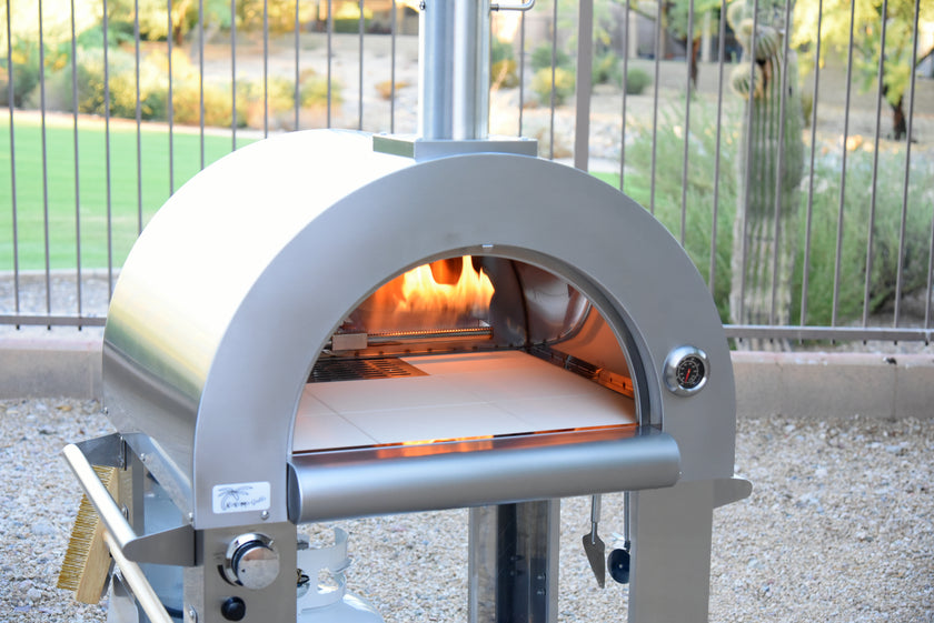 Outdoor pizza oven with fire inside, set against a garden background