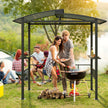 People grilling outdoors under a metal gazebo with a scenic background