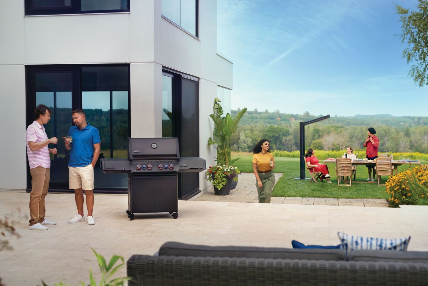 People socializing outdoors with a barbecue grill in a modern backyard setting.