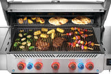 Stainless steel grill with various foods being cooked on different grates.