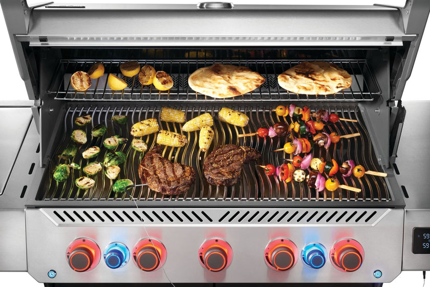 Stainless steel grill with various foods being cooked on different grates.