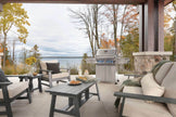Outdoor patio with chairs, table, and grill overlooking a lake and trees.
