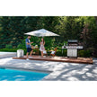 Two people by a poolside with a grill and umbrella