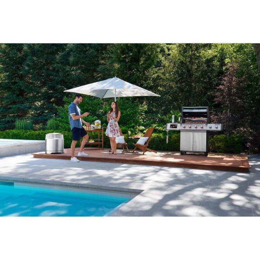 Two people by a poolside with a grill and umbrella