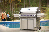 Stainless steel grill on a patio with people and a pool in the background