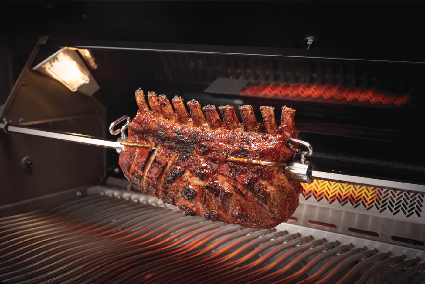 Grilled rack of lamb on a rotisserie over an open grill.