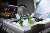 Green bottles with white caps in a cooler next to a grill and laptop displaying a menu.