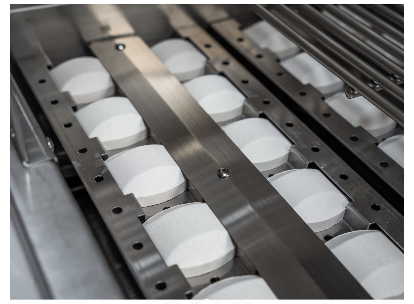 Row of white cylindrical objects on a metal conveyor belt