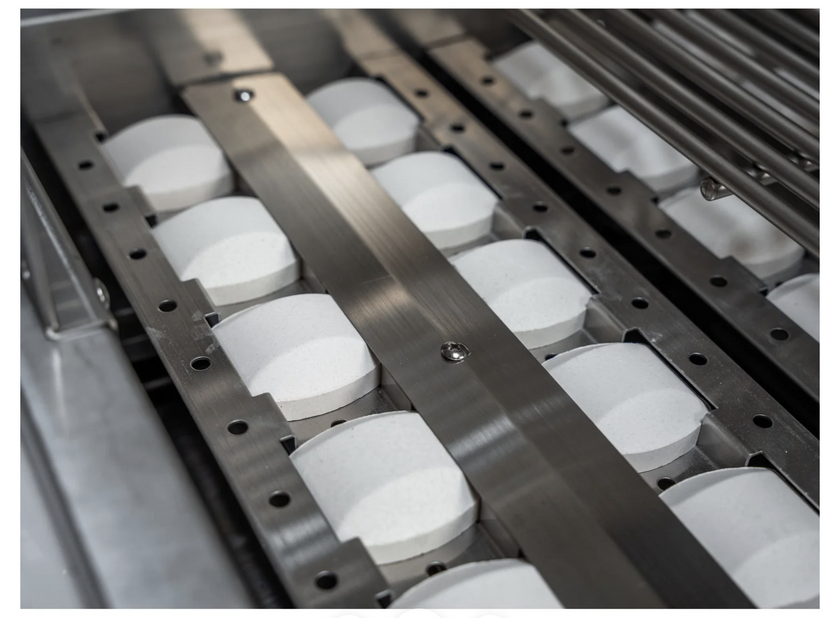 Row of white cylindrical objects on a metal conveyor belt
